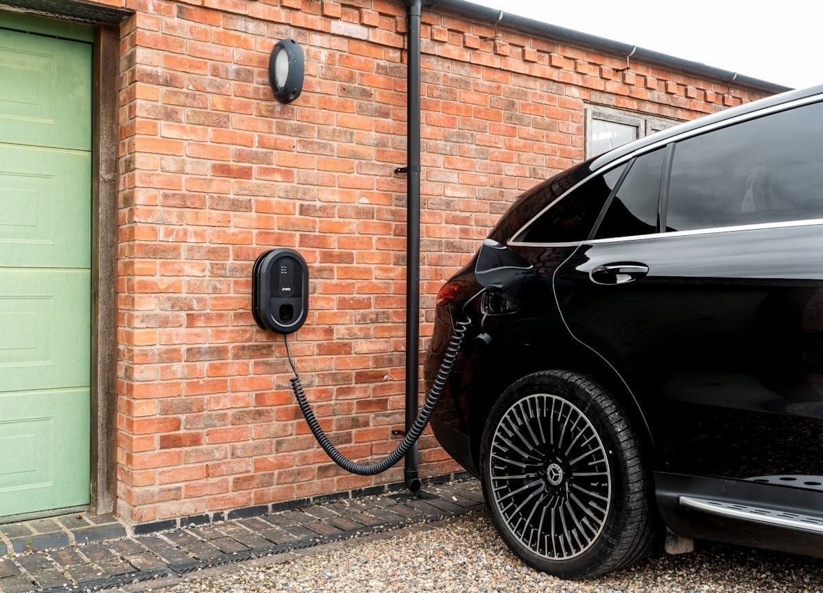 Ein schwarzes Elektroauto lädt an einer wandmontierten Ladestation neben einer Backsteinwand